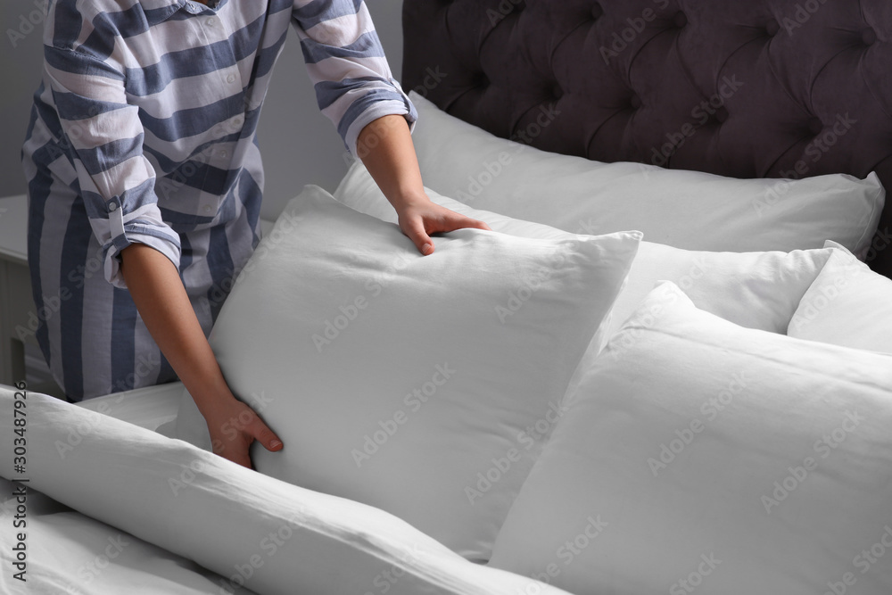 Woman fluffing white pillow on bed, closeup