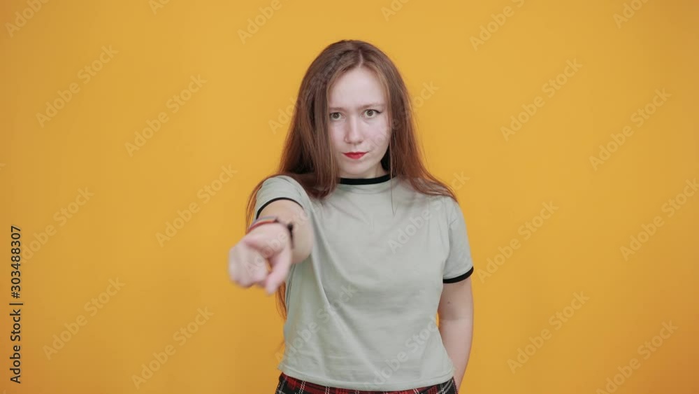 Beautiful brunette caucasian young lady wearing pretty shirt staying over isolation orange background pointing away her finger into distance directly, having rainbow bracelet on hand Beautiful brunette caucasian young lady wearing pretty shirt staying over isolation orange background pointing away her finger into distance directly, having rainbow bracelet on hand