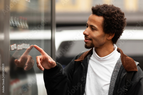 African man buys drink or sweets at vending machine outside.