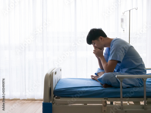Depression disorder patient asian young male sitting alone and thinking about his life and live on hospital bed with blue uniform in the special VIP room