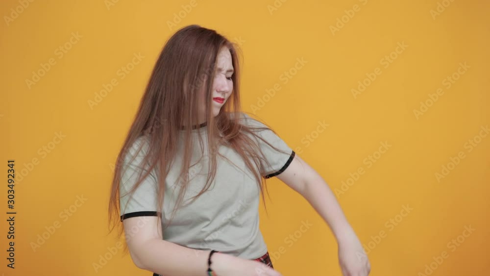 Relaxed young woman in casual clothes keeping head aside, with hand on forehead isolated on orange wall background in studio. People sincere emotions, lifestyle concept. Relaxed young woman in casual clothes keeping head aside, with hand on forehead isolated on orange wall background in studio. People sincere emotions, lifestyle concept.