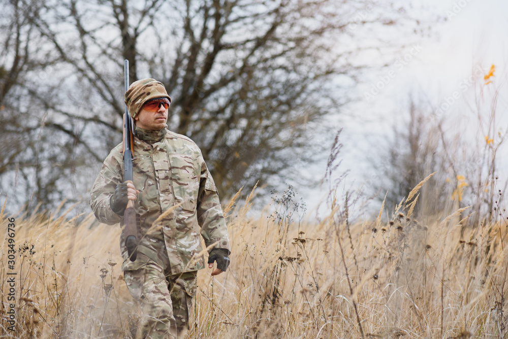 Obraz premium hunting, war, army and people concept - young soldier, ranger or hunter with gun walking in forest