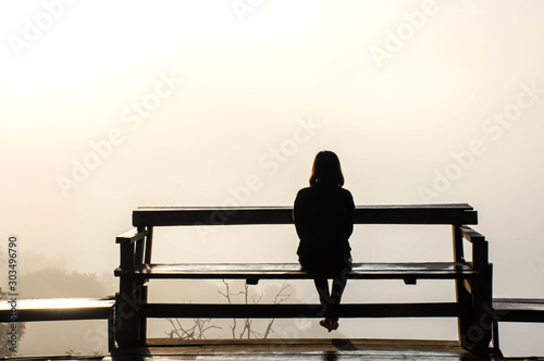 The image behind Woman sitting on a wooden chair Background fog  and morning sunlight.