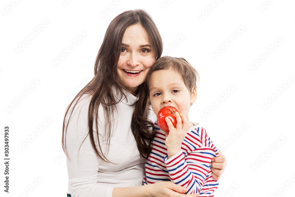 Young smiling mom with a son are vegetarians. The boy is eating a juicy tomato. Isolated over white background. Young smiling mom with a son are vegetarians. The boy is eating a juicy tomato. Isolated over white background.