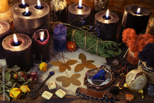 Still life with black candles, runes, crystals and four leaf clover on witch table.
