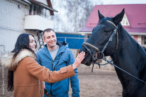 Couple in love on a walk with a black horse at the racetrack.