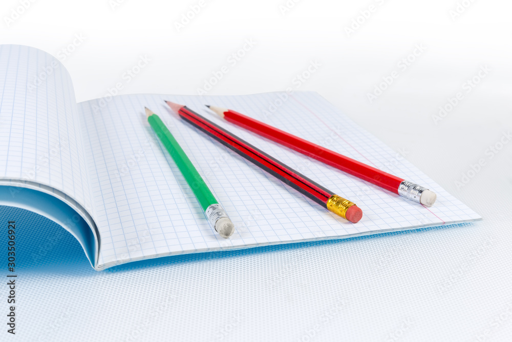 Different graphite pencils with erasers on open exercise book closeup Different graphite pencils with erasers on open exercise book closeup