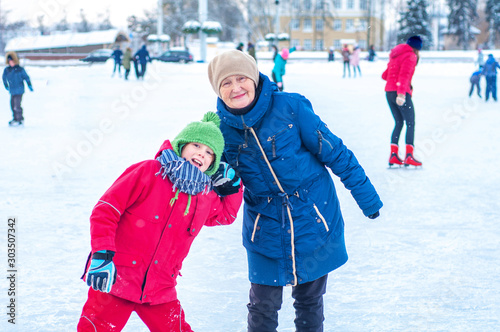 Grandmother and grandson granddaughter ride on a city ice rink holding hands. Happy winter holidays. Winter outdoor activities