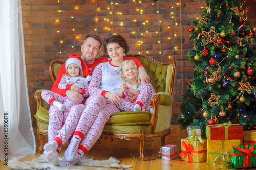 Portrait of a happy family sitting in pajamas in a chair near the festive Christmas tree and hugging and smiling. Christmas morning