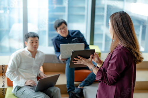 Business meeting and teamwork concept. Asian businesswoman explaining project data report to colleagues using digital tablet for presentation at workplace. Coworkers team brainstorming ideas in office