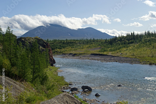 Kozhim River. A high cliff on one side of the river and a gentle wooded shore on the other side. A mountain is visible in the distance. A clear sunny day. Subpolar Ural, Yugyd Va National Park © Алексей Перетягин