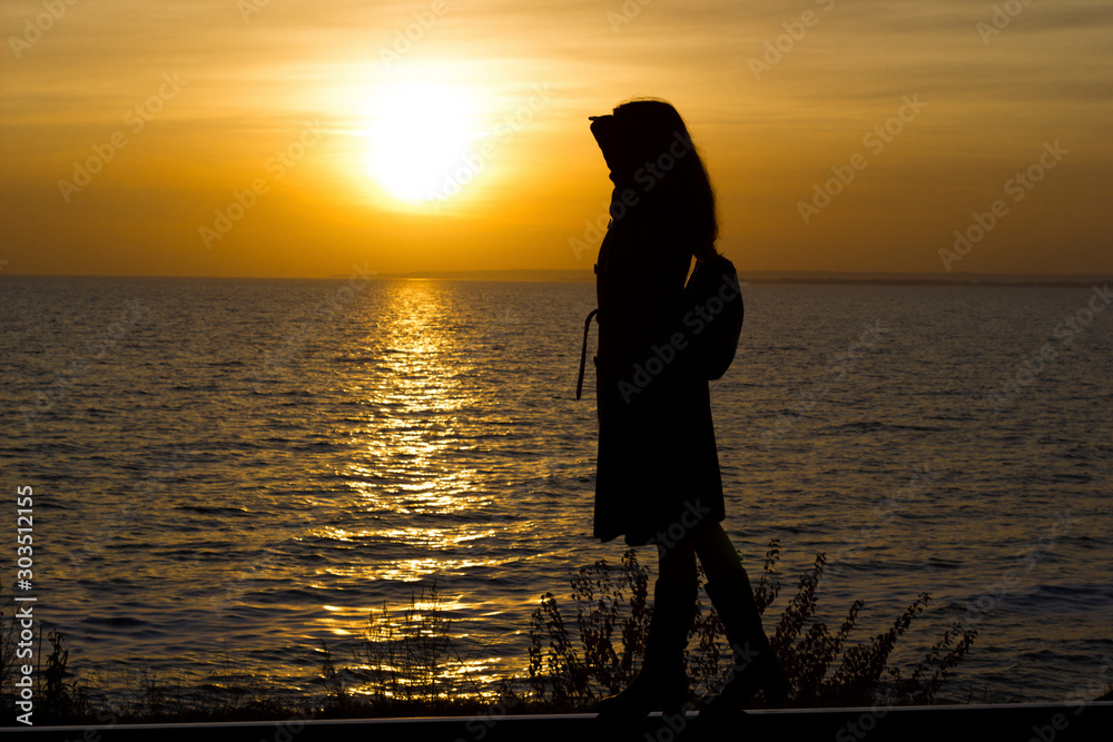 Girl walks on railroad tracks in coat on sunset background