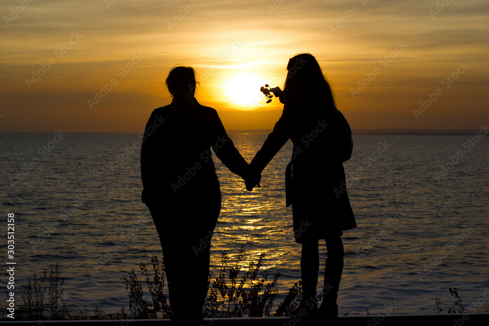 Girlfriends standing on railway rails holding hands on sunset background