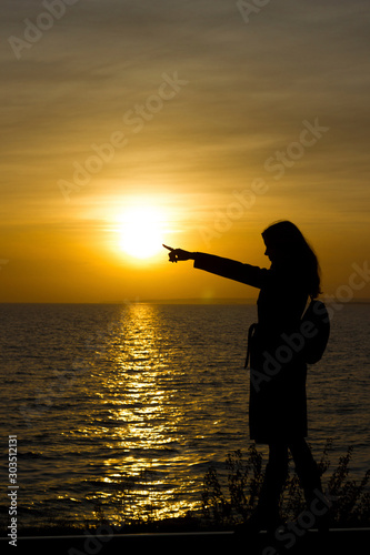 Girl walks on railroad tracks in coat indicate, point on sunset background