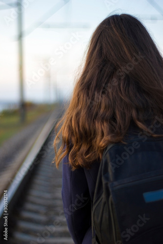 Girl walks on railway rails in a coat - travel, lifestyle