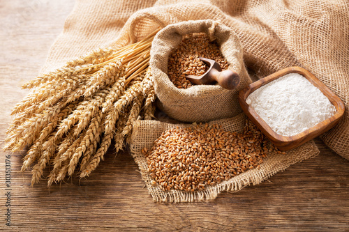 Fotografia wheat ears, grains and bowl of flour on a wooden table