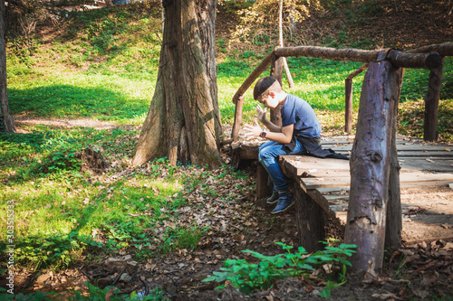 Little boy sitting on wooden bridge in nature.