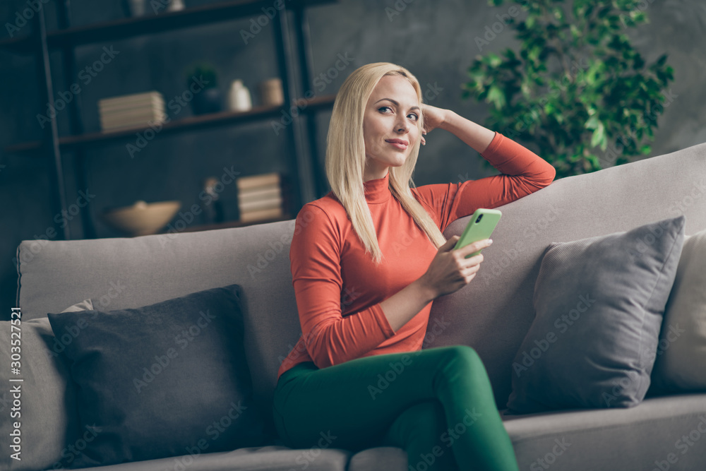 Obraz premium Photo of pretty blonde lady domestic mood holding telephone imagination flight think over new creative post text sitting comfy couch casual outfit living room indoors