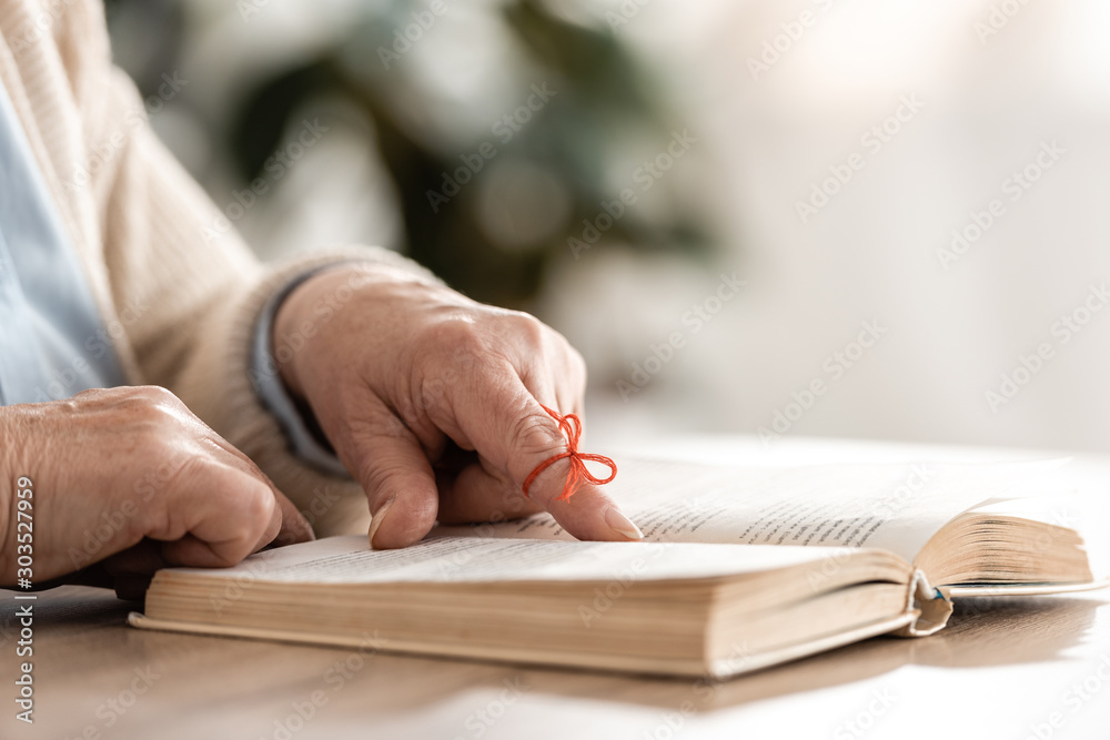cropped view of senior woman with red bow on finger pointing with finger at book cropped view of senior woman with red bow on finger pointing with finger at book