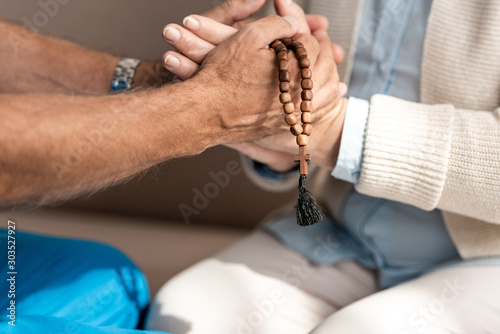 cropped view of doctor with rosary beads holding hands of senior woman