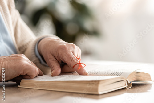 cropped view of senior woman with red bow on finger pointing with finger at book