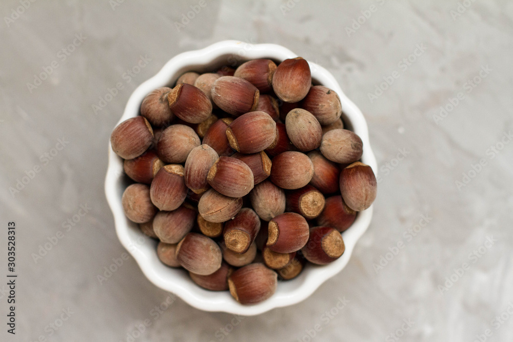 Hazelnuts, lots of hazelnuts in a white plate on a grey wooden background. Hazelnut background, healthy food. space for text. space for copy on the banner. Hazelnuts, lots of hazelnuts in a white plate on a grey wooden background. Hazelnut background, healthy food. space for text. space for copy on the banner.