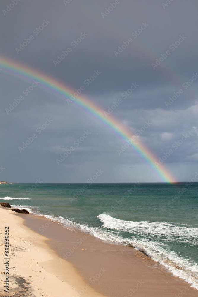 Sardinian coast, rough sea and cloudy sky after the rain with a rainbow that is born on the sea. Rainbow over the sea after a heavy rain. Abnormal rains and storms on the Mediterranean sea Sardinian coast, rough sea and cloudy sky after the rain with a rainbow that is born on the sea. Rainbow over the sea after a heavy rain. Abnormal rains and storms on the Mediterranean sea