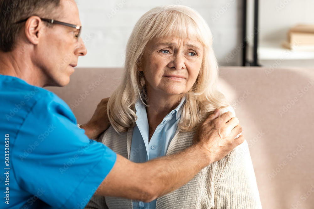 Fototapeta premium selective focus of doctor in glasses touching upset senior woman