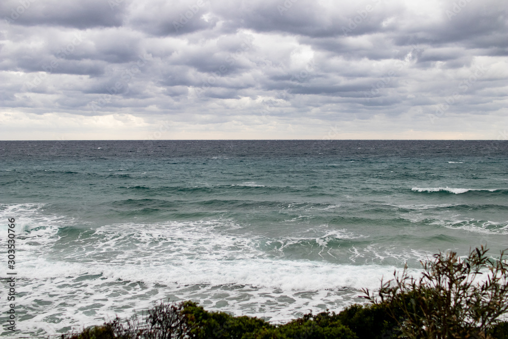 stormy sea on the Mediterranean coast, rain on the sea with high waves, abnormal storm and waves with shiuma, cloudy sky and cold colors