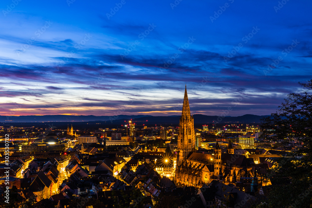 Germany, Big city lights of freiburg im breisgau skyline and cityscape illuminated by night in magical twilight after sunset, aerial view from above the roofs