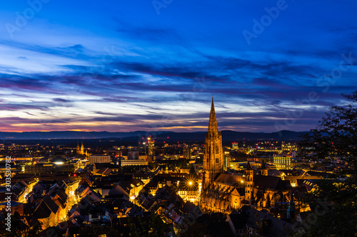 Germany, Big city lights of freiburg im breisgau skyline and cityscape illuminated by night in magical twilight after sunset, aerial view from above the roofs