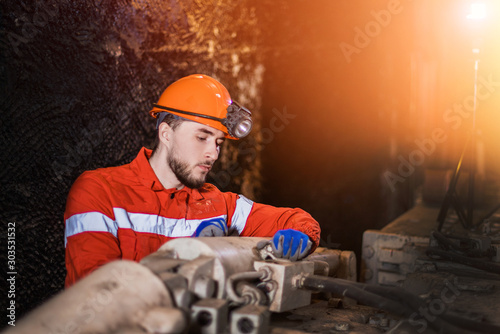 profession of a miner. A young miner in a coal mine in the generals is busy with work, repairing against a background of technology. mine equipment. Portrait. red shape.