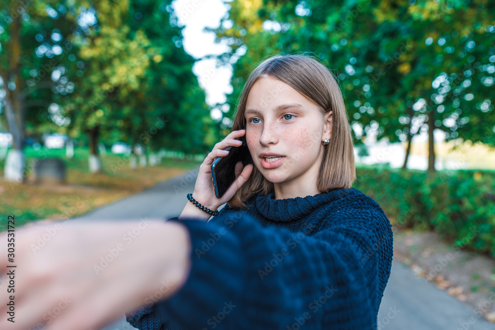teenager girl holding mobile phone in her hands, in summer in city, autumn day funny and hand gesture calls and talks, listens to voice message in Internet application. teenager girl holding mobile phone in her hands, in summer in city, autumn day funny and hand gesture calls and talks, listens to voice message in Internet application.