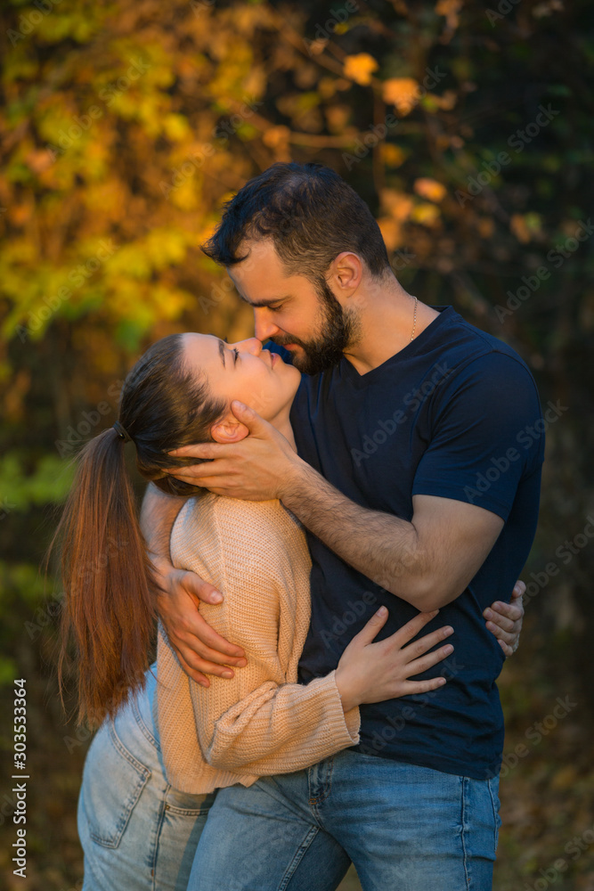 Young couple in love hugging and kissing in the Park. They are illuminated by a ray of sunlight. In the background autumn forest. Young couple in love hugging and kissing in the Park. They are illuminated by a ray of sunlight. In the background autumn forest.