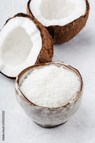 health content, broken coconut halves and coconut shavings in a bowl, light gray background, vertical