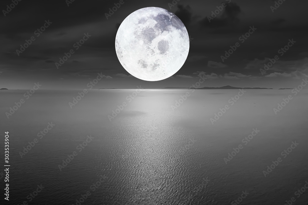 Aerial view Dramatic atmosphere of peaceful black and white image of the ocean with beautiful bright full moon and dark sky background. Image of moon furnished by NASA.