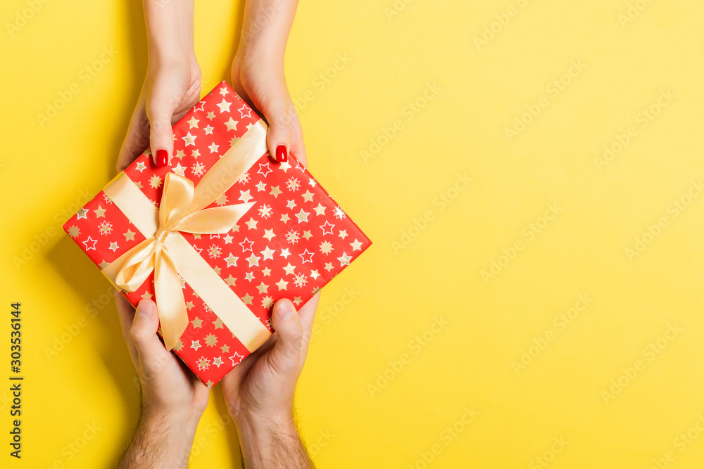 Top view of a man and a woman giving and receiving gift for a holiday on colorful background. Love and relationship concept with copy space - obrazy, fototapety, plakaty 