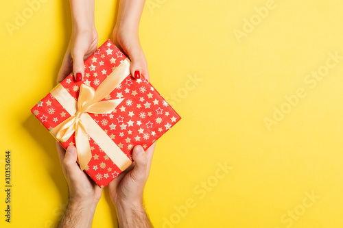 Top view of a man and a woman giving and receiving gift for a holiday on colorful background. Love and relationship concept with copy space