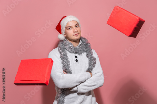 Handsome man in a white sweater, Santa hat and trumpery shows magic making Christmas gifts livitate around him. photo