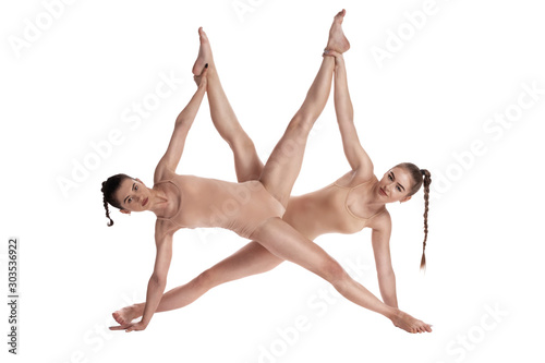 Two flexible girls gymnasts in beige leotards performing complex elements of gymnastics using support, posing isolated on white background. Close-up.