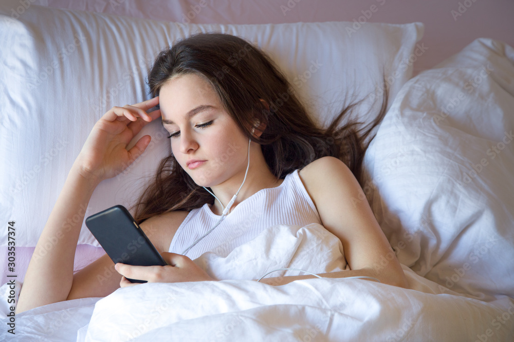 Teen girl using cell phone on waking feels good in the morning on the bed Teen girl using cell phone on waking feels good in the morning on the bed