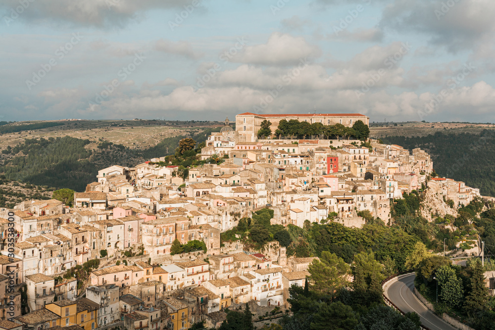 sunlight on small houses and green trees on hill in ragusa, italy