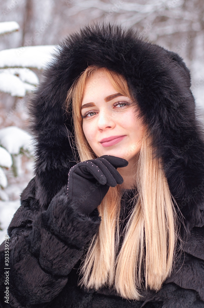 Young pretty girl of model appearance in a natural black fur coat basks in the snowy winter. Fashion. Style. Winter clothes made of natural fur. Fur coats. Gloves. Young pretty girl of model appearance in a natural black fur coat basks in the snowy winter. Fashion. Style. Winter clothes made of natural fur. Fur coats. Gloves.