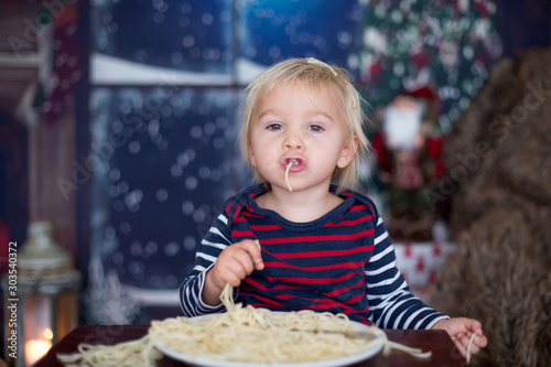 Sweet toddler child, boy, eating spaghetti at home