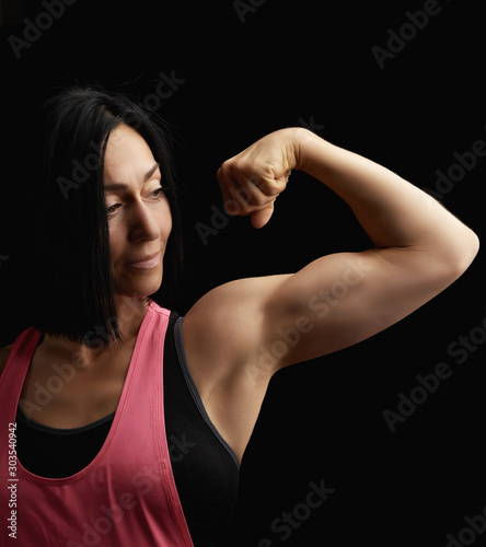 beautiful athletic girl raised and bent her arm demonstrating her biceps, athlete is standing on a dark background
