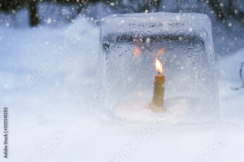Winter lantern made of ice, burning candle inside, in snowfall.