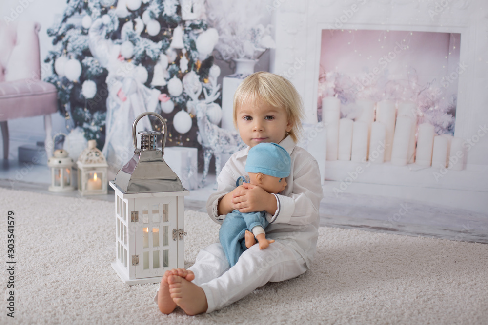 Fototapeta premium Beautiful blonde toddler boy, dressed in white in decorated white room for Christmas