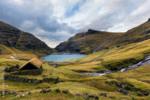 Saksun village and sandy shore of the lagoon with an azure lake and dramatic clouds. Island Streymoy, Faroe Islands. Europe