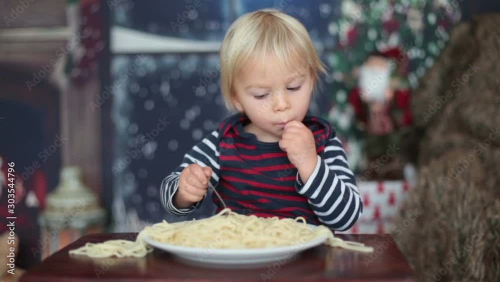 Sweet toddler child, boy, eating spaghetti at home on Christmas