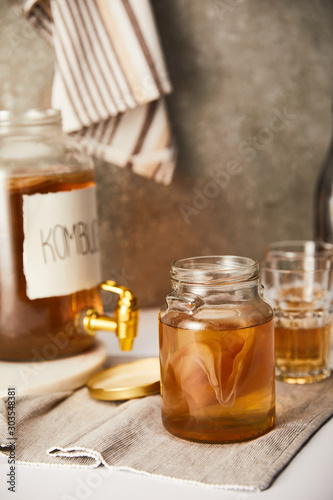 selective focus of jar with kombucha near glasses on textured grey background with striped napkin